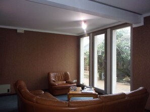 A living room with a brown leather sofa, a wooden coffee table, and a brown leather armchair. There is a large window with a view of greenery outside. - Jackotel Orleans (Orléans)