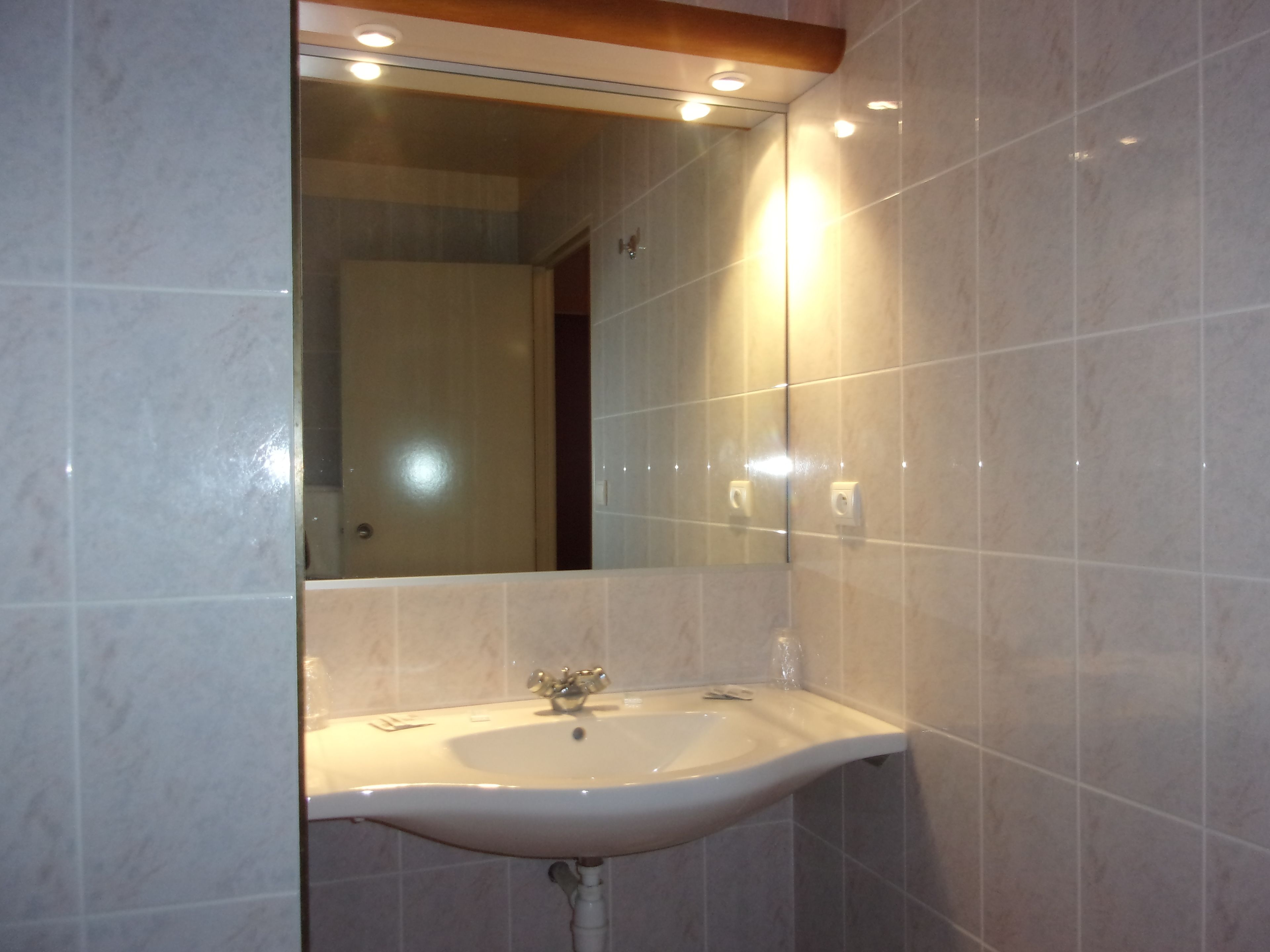 A bathroom with a white sink, a mirror above it, and tiled walls.