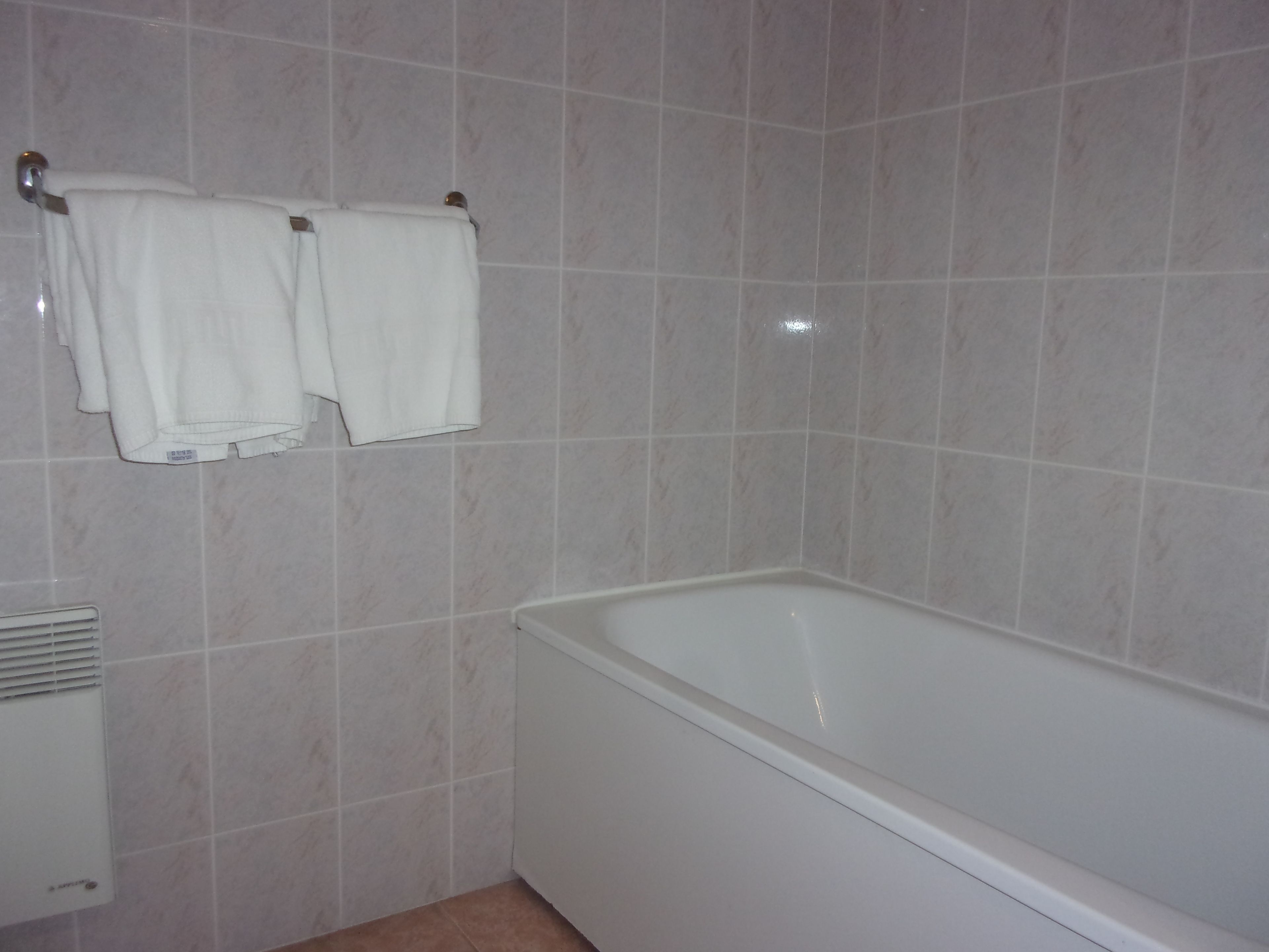 Un baño con bañera, paredes de azulejos y dos toallas colgadas en un perchero.