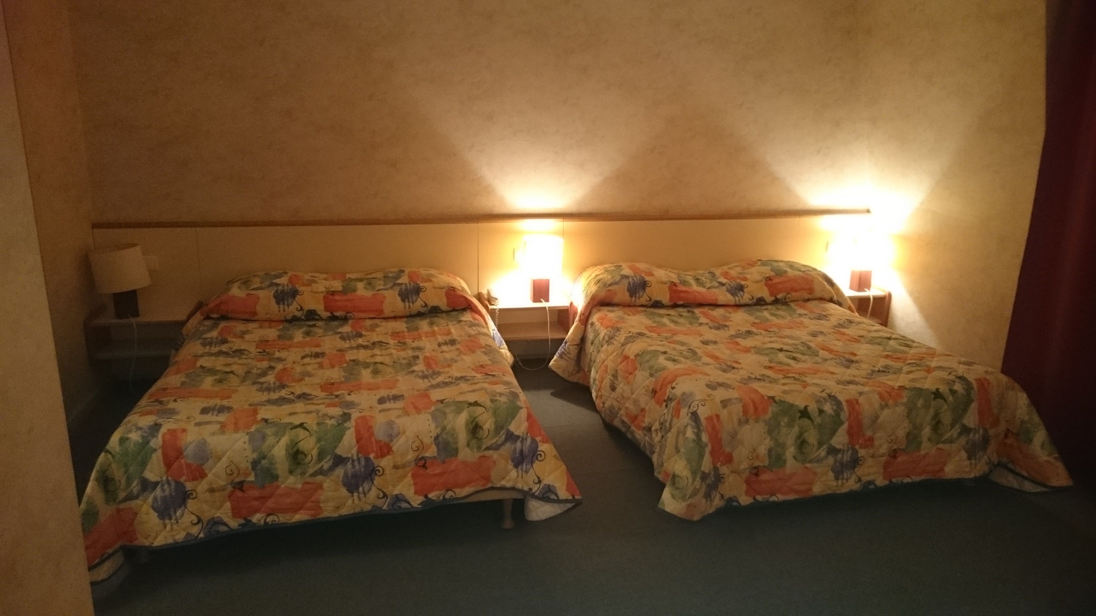Habitació amb dos llits, cadascun amb un estenat estampat, taules de nit amb làmpades i un taulell.