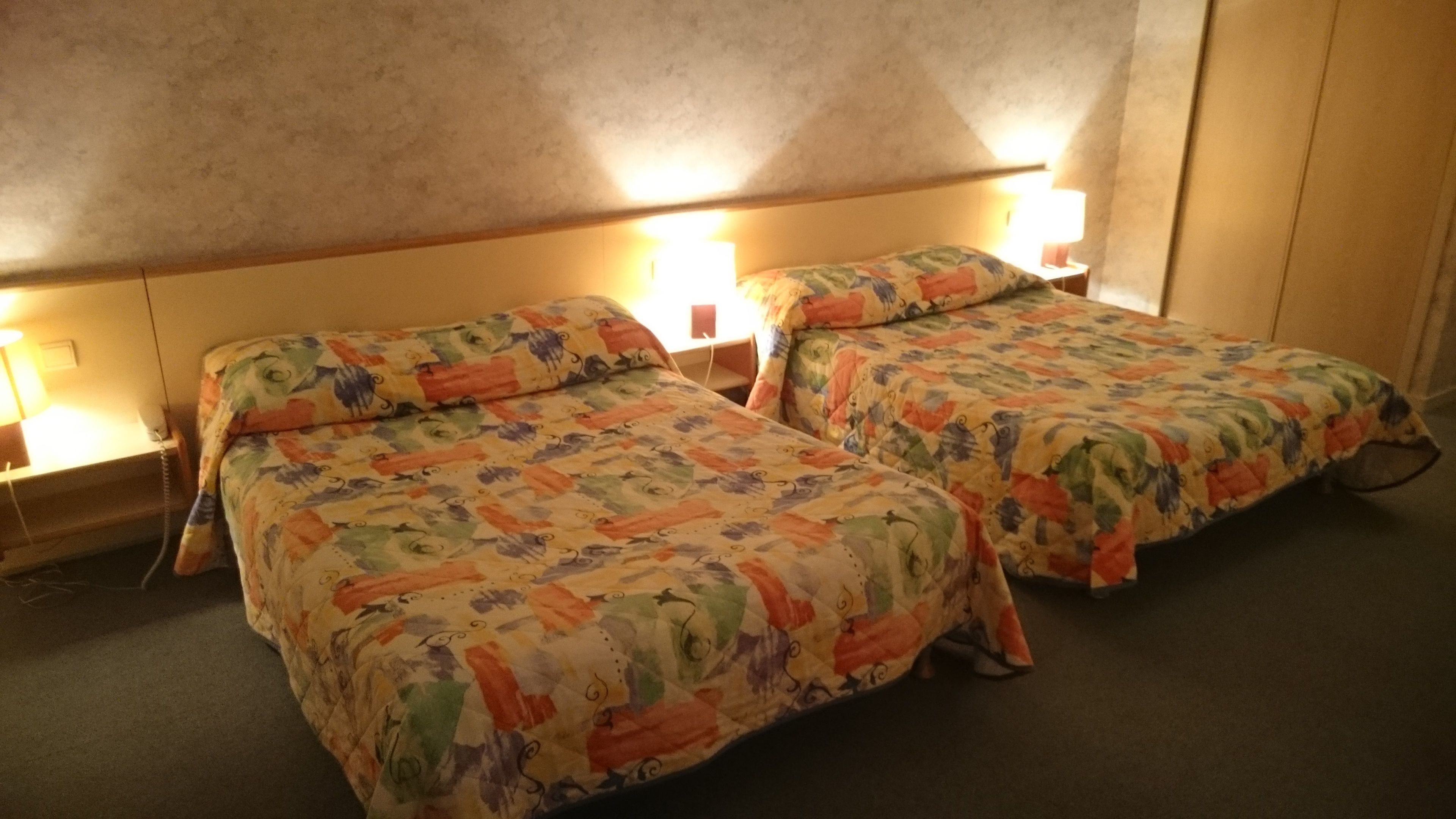 Une chambre d’hôtel avec deux lits, chacun agrémenté de draps à motifs floraux et de lampes de chevet.