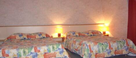 A hotel room with two beds, each with a patterned bedspread, two bedside lamps, and a red curtain.