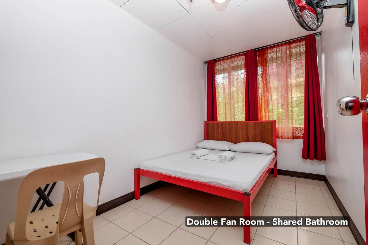 A double fan room with a bed, a chair, and a window with curtains.