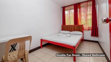 Habitación doble con ventiladores, una cama, una silla y un ventanal con cortinas.