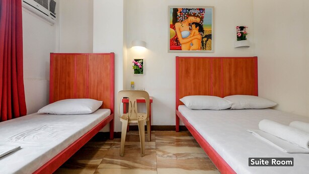 A suite room with two single beds, a chair, a small table, and a wall-mounted air conditioner. - Stay Malate Hostel (Manila)