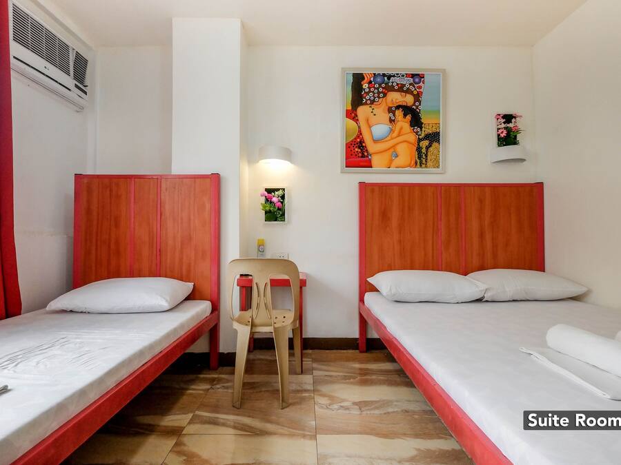 Una suite con dos camas individuales, una silla, una mesita y aire acondicionado instalado en la pared.