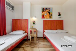 Una suite con dos camas individuales, una silla, una mesita y aire acondicionado instalado en la pared.
