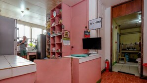 A pink reception desk with a 'Pay here' sign, shelves with various items, and a visible kitchen area in the background. - Stay Malate Hostel (Manila)