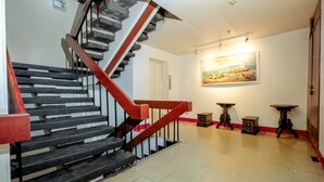 A staircase with black steps and a red handrail, leading to a room with a painting on the wall and three small tables. - Stay Malate Hostel (Manila)