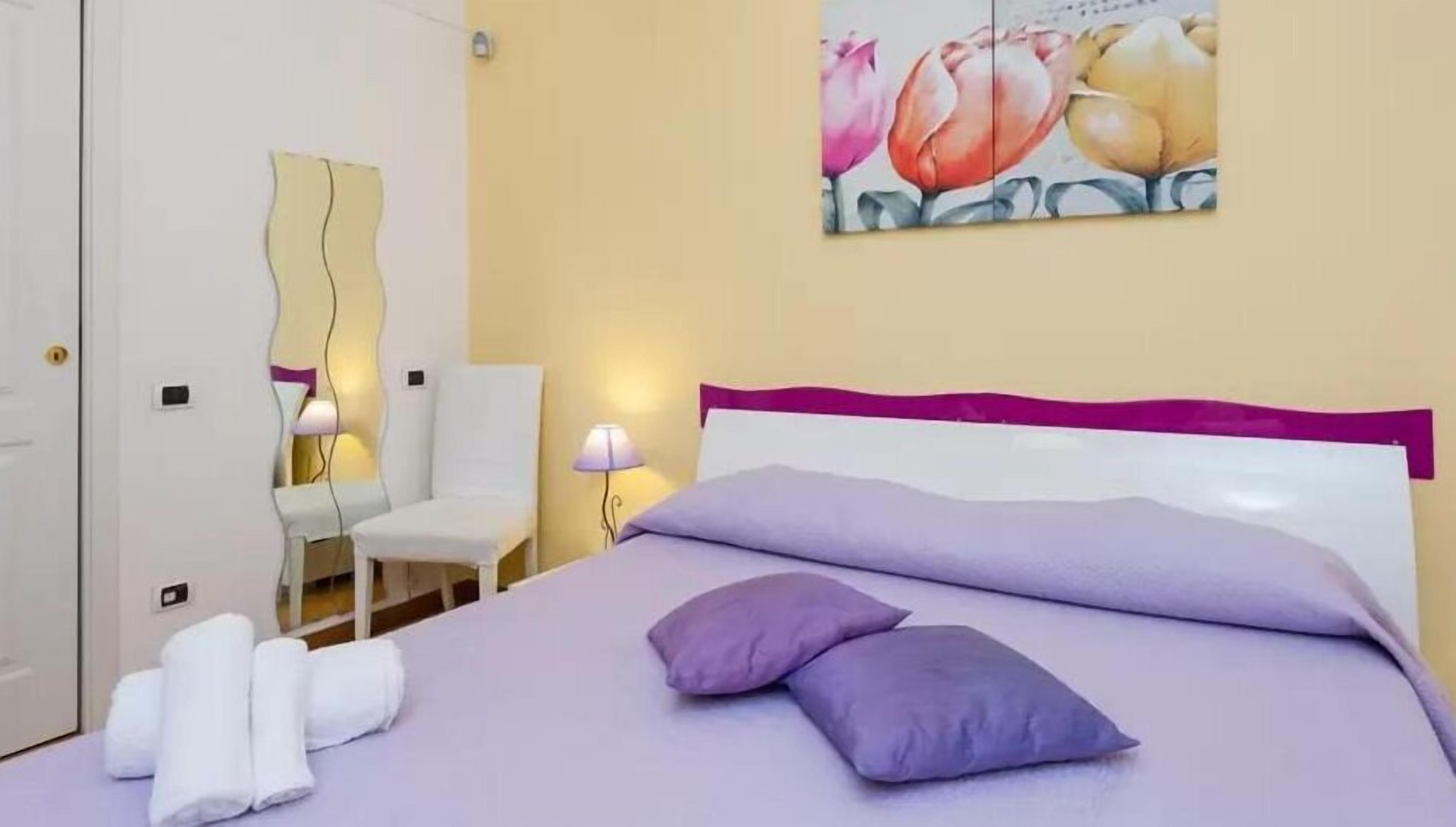 Ein Hotelzimmer mit einem Bett, einem Sessel und einem Blumengemälde an der Wand.