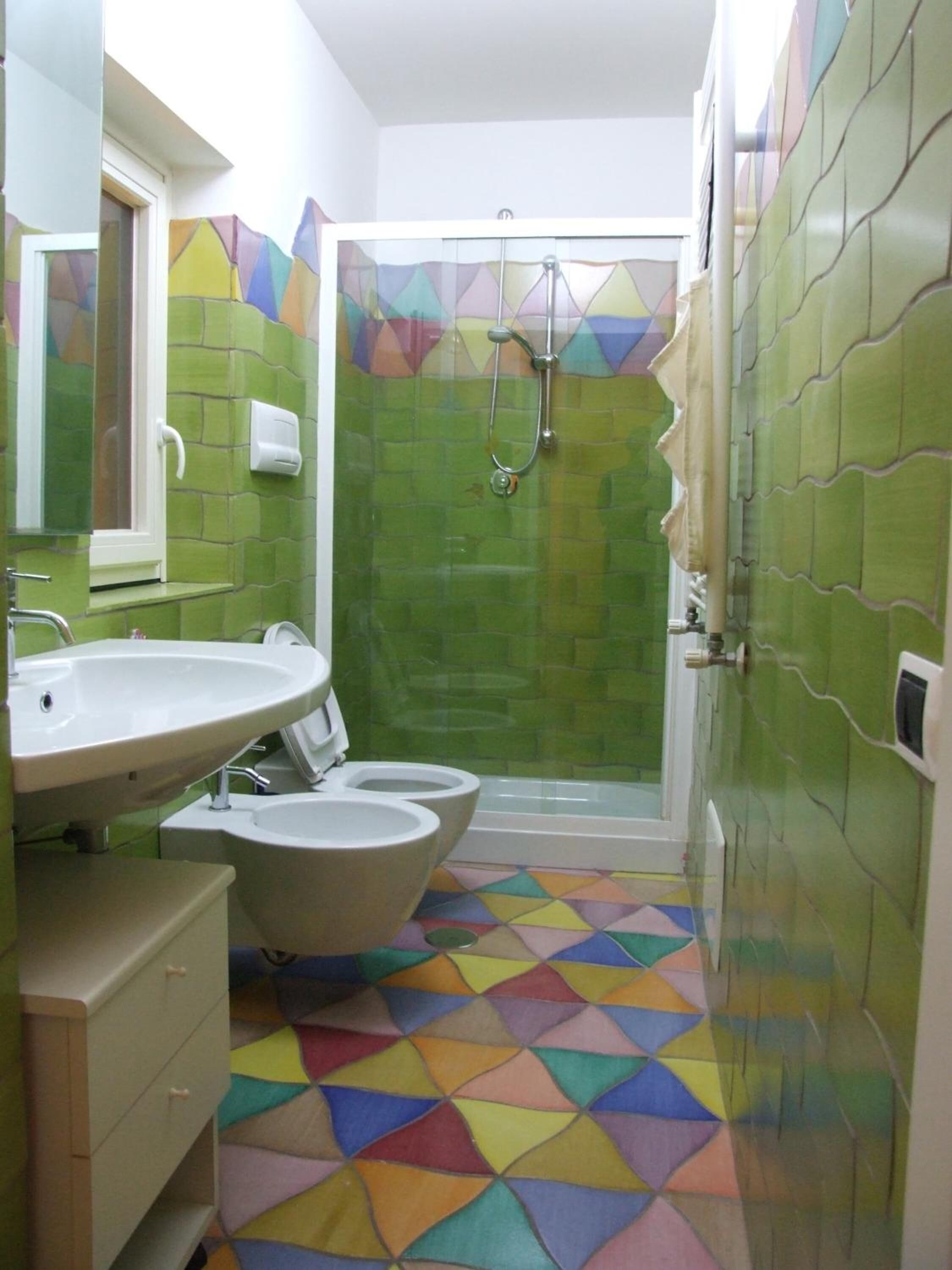 A bathroom with a sink, two toilets, a shower, and a colorful geometric floor pattern.