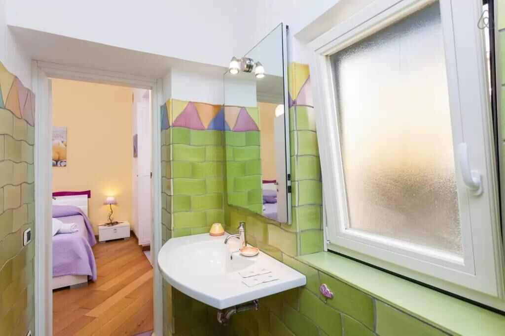 A bathroom with a white sink, green tiled walls, a mirror, and a frosted window.