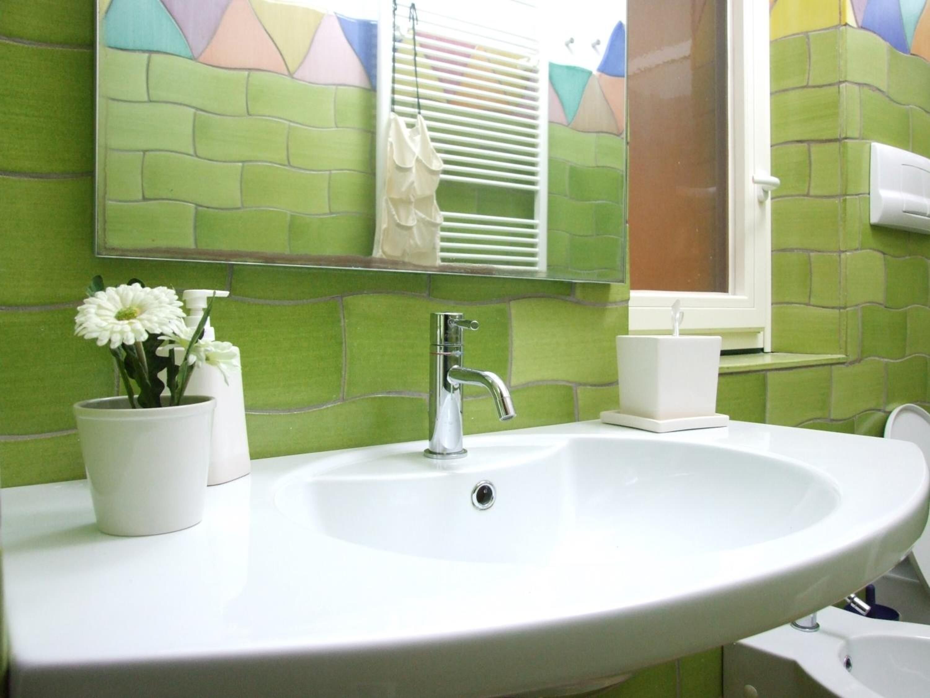 Een badkamer met een witte wastafel, een spiegel en groene betegelde wanden.