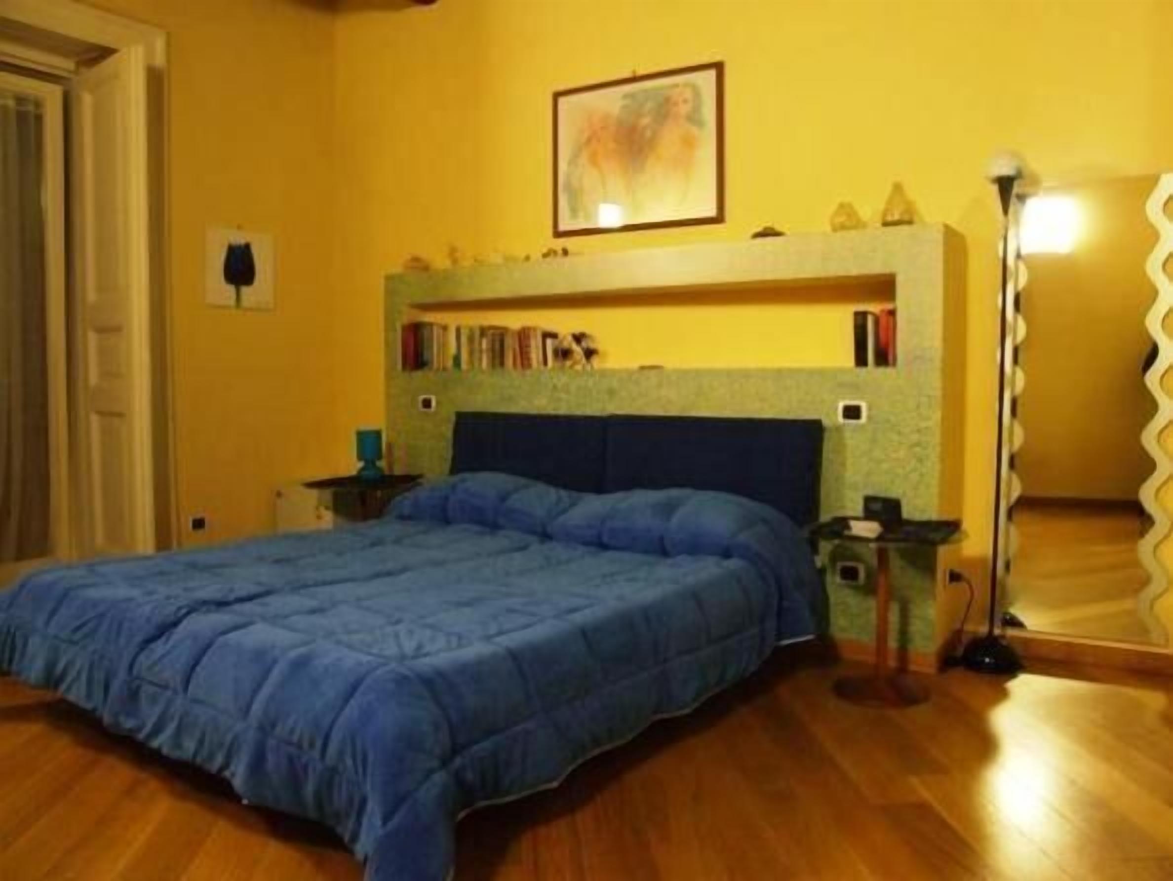 A bedroom with a bed, a bookshelf, a floor lamp, and a mirror.