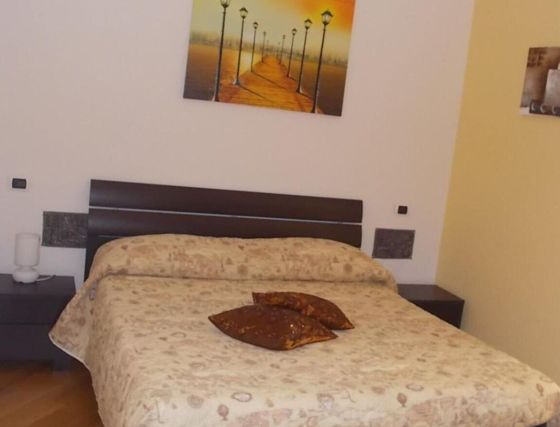 A bedroom with a bed, a nightstand, a wall-mounted lamp, and a painting.