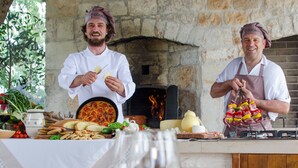 Cocineros preparando comida en una cocina al aire libre con una pared de piedra y un horno de leña.