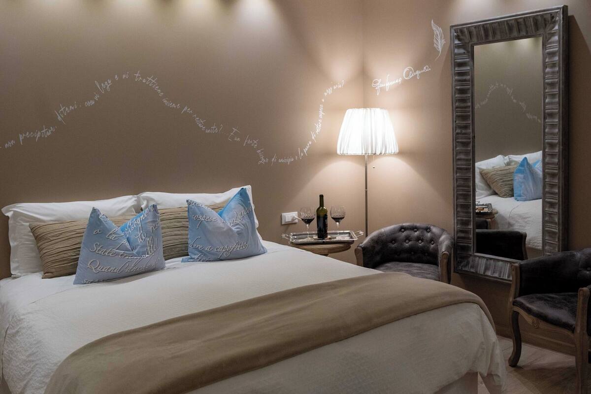 A well-lit bedroom with a large bed, bedside tables, a mirror, and a lamp.