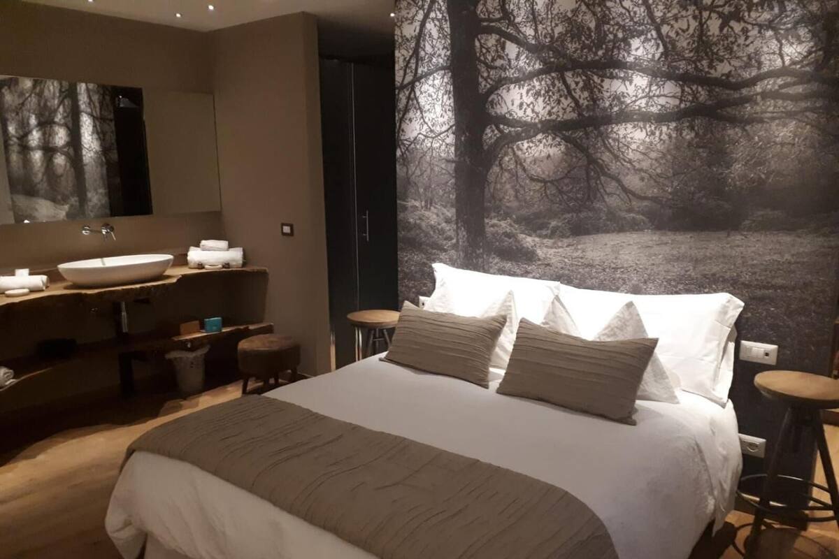 A modern bedroom with a large bed, a vanity with a mirror, and a wall mural of trees.