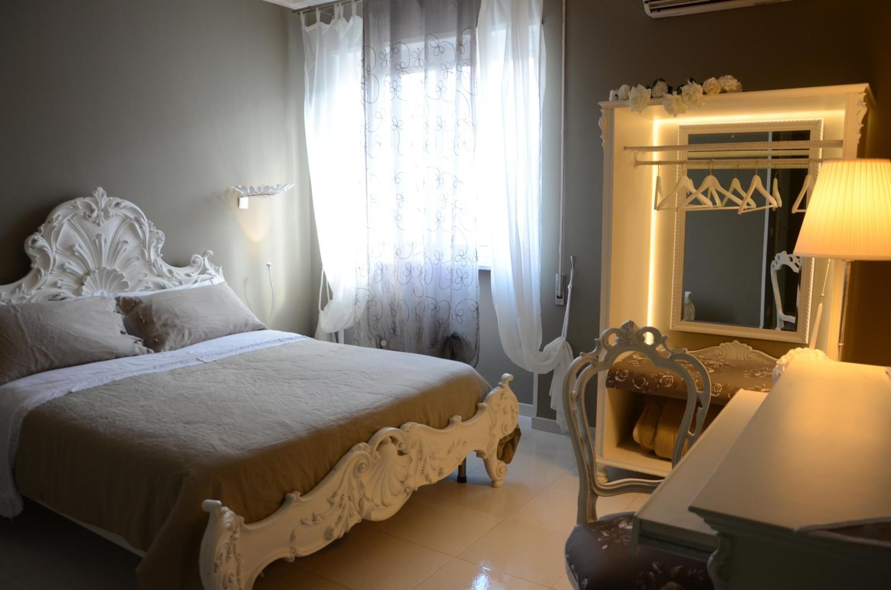 A bedroom with a large bed, a mirror with a light, and a chair.