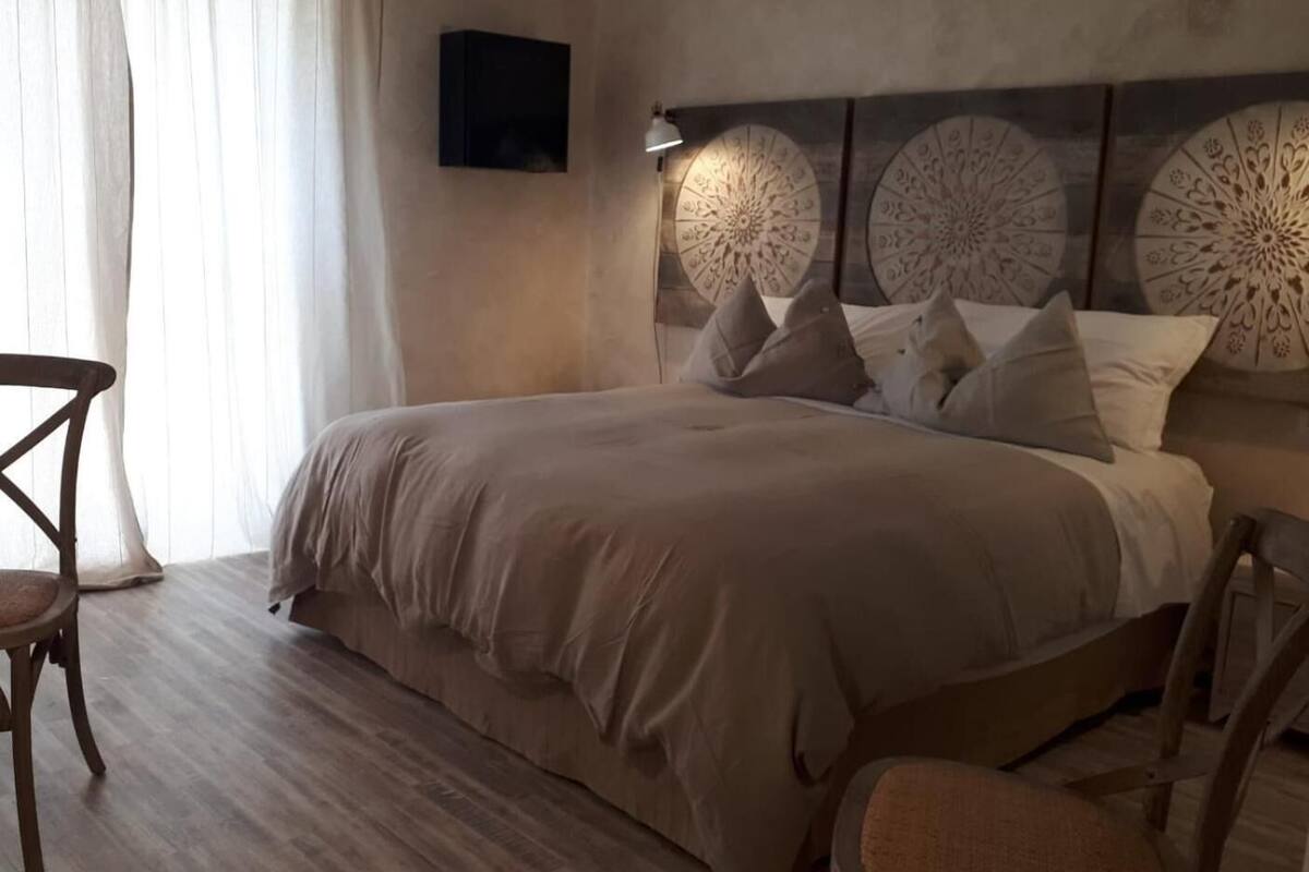 A bedroom with a large bed, two bedside tables, a chair, and a wall-mounted TV.