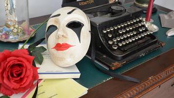 A vintage Remtor typewriter on a wooden desk with a decorative mask, a red rose, and some papers.