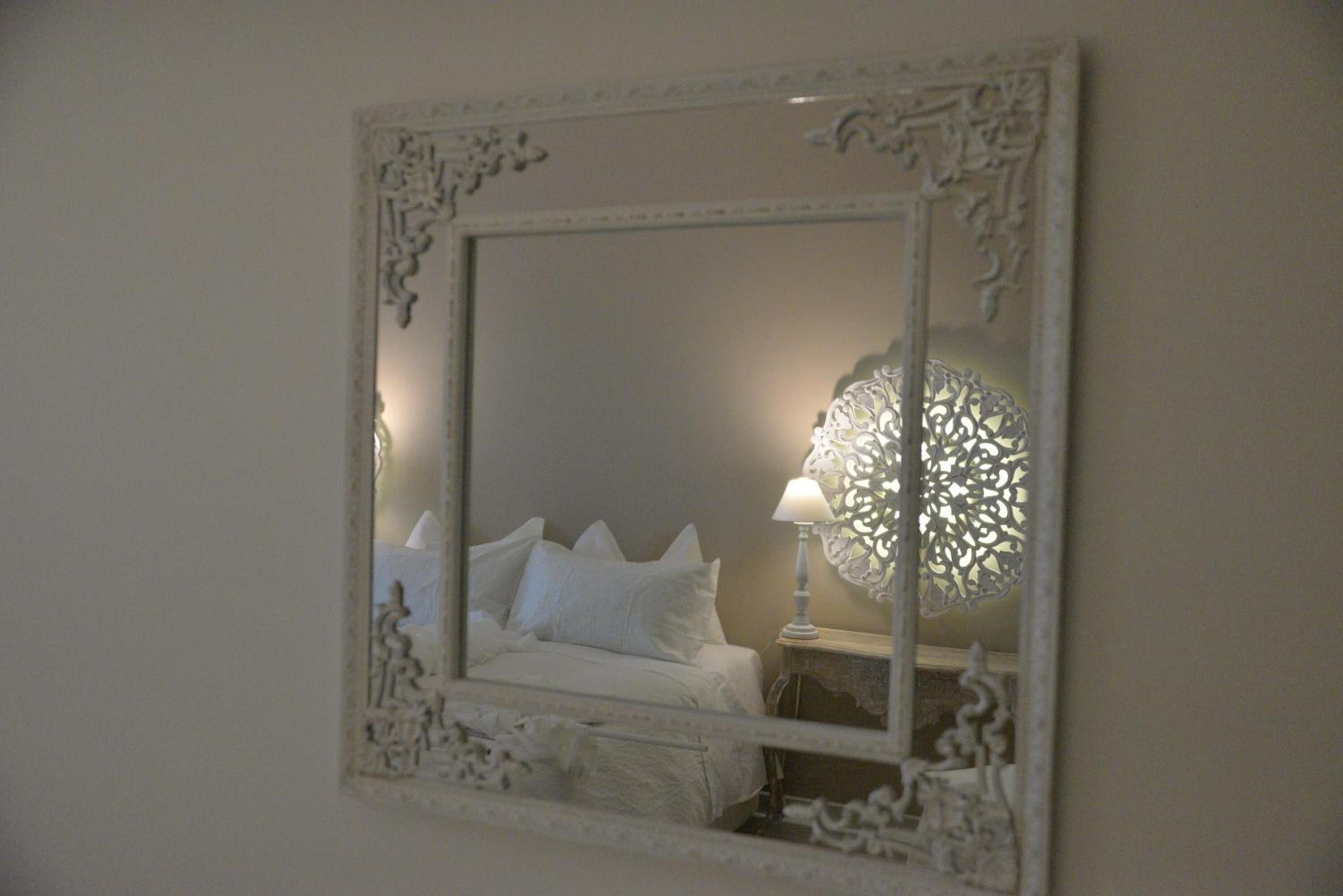 A bedroom with a bed, a nightstand, and a decorative wall mirror.
