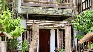 A wooden entrance with a thatched roof structure, surrounded by lush greenery and a wooden fence. - Little Prince Resort & Spa (Siem Reap)