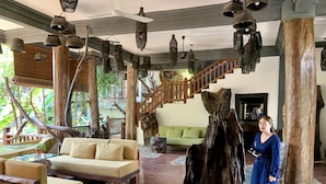 A spacious lobby with a wooden floor, a green sofa, and a large tree stump centerpiece. - Little Prince Resort & Spa (Siem Reap)