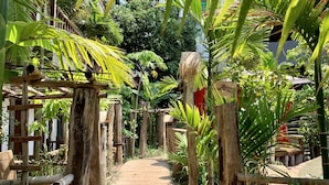 A wooden pathway flanked by bamboo structures and lush greenery, leading to a building with a thatched roof. - Little Prince Resort & Spa (Siem Reap)