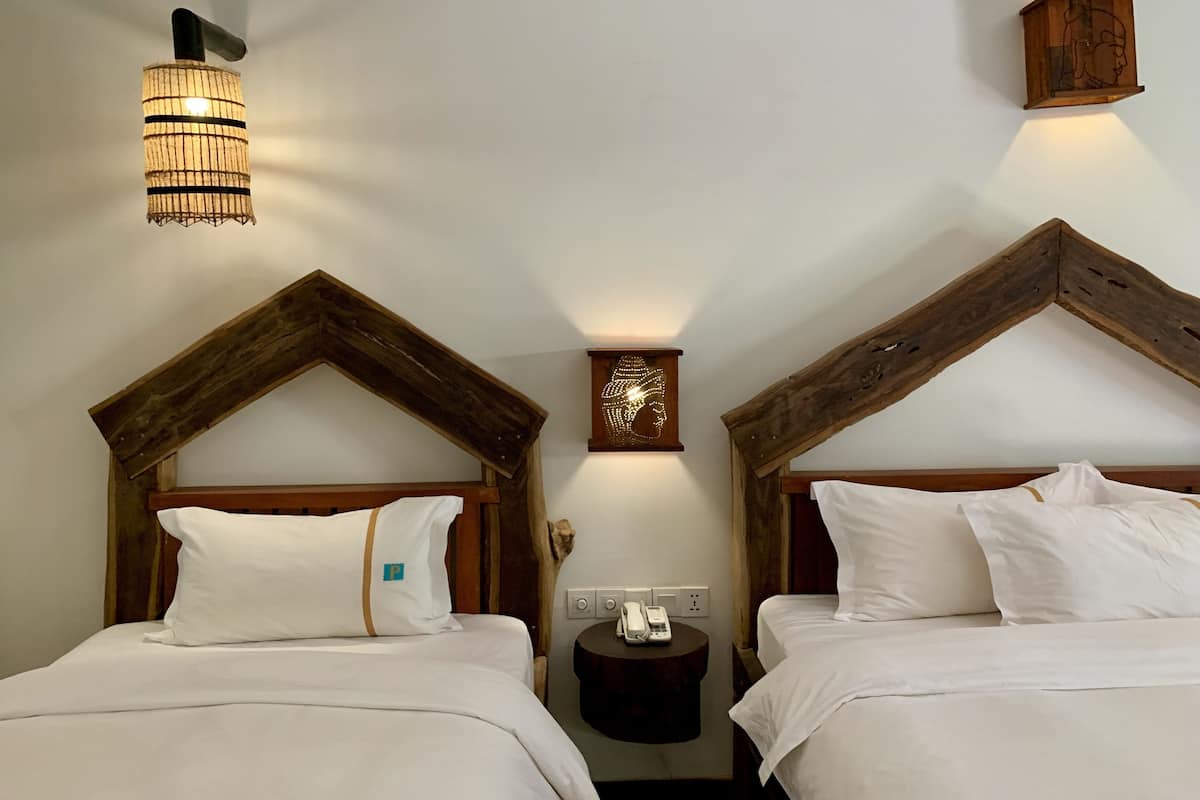 Ein Hotelzimmer mit zwei Betten, Holz-Kopfteilen, einem Nachttisch, einer Wandleuchte und einem Wandbild.