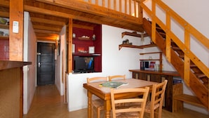 Une table de salle à manger en bois, accompagnée de quatre chaises, un coin cuisine avec un téléviseur et un escalier en bois.