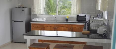 Una cocina con una isla central, armarios de madera, un refrigerador, una ventana con cortinas y vistas al exterior.