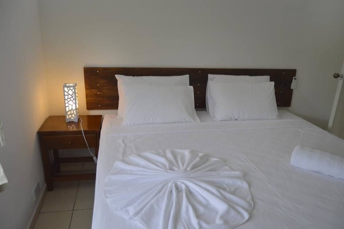 A neatly made bed with white linens, a wooden headboard, and a bedside table with a lamp.
