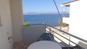 Un balcón con una mesa blanca y sillas azules, con vistas a una playa y al mar.