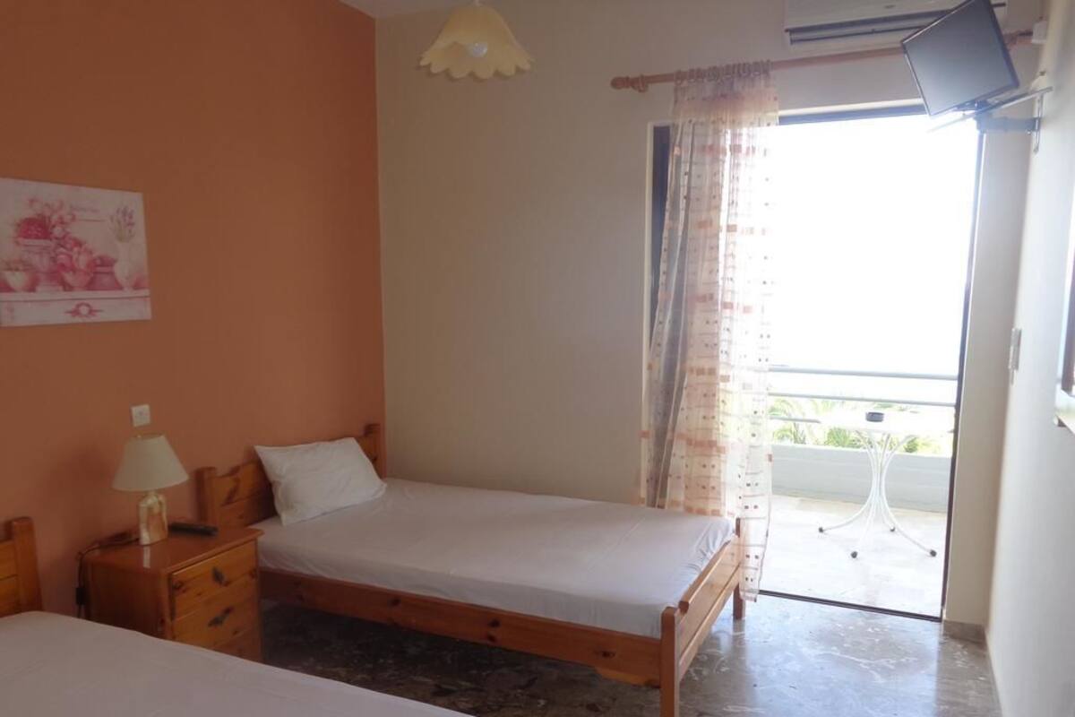 A room with two wooden beds, a small table with a lamp, a ceiling fan, and a window with curtains.