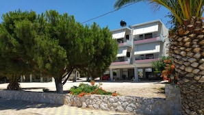 Un edificio de varios pisos con techo plano, pared de piedra y un árbol en primer plano.