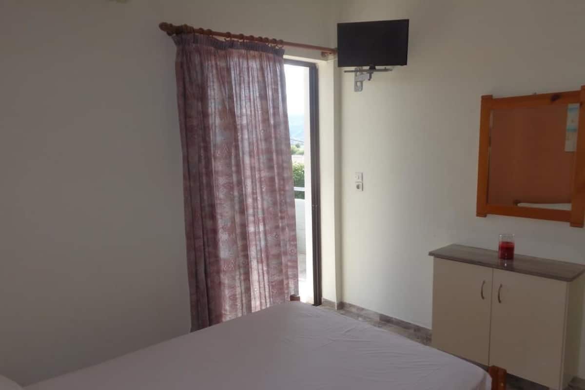A bedroom with a bed, a television mounted on the wall, a cabinet, and a window with curtains.
