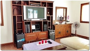 A living room with a TV, entertainment system, wooden cabinets, a dining table with a mat, and a sofa.