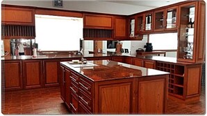 A spacious kitchen with wooden cabinetry, a central island, and a built-in wine rack. - Wongsuwan Pool Villa (Hua Hin)