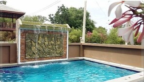 A swimming pool with a stone wall and a covered area.