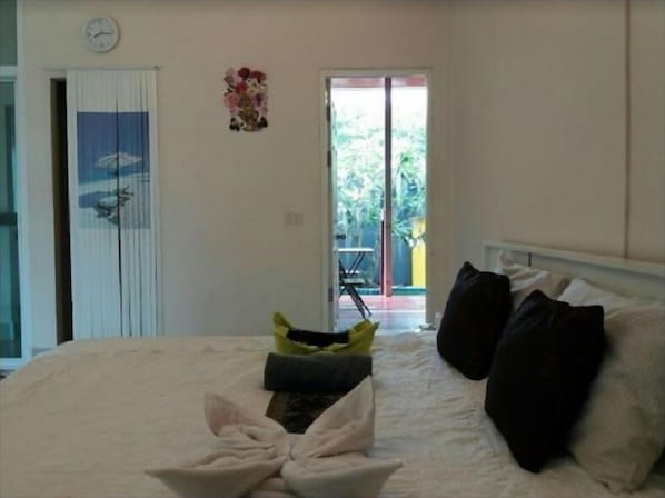 A bedroom with a bed, pillows, a clock, and a door leading to a balcony.
