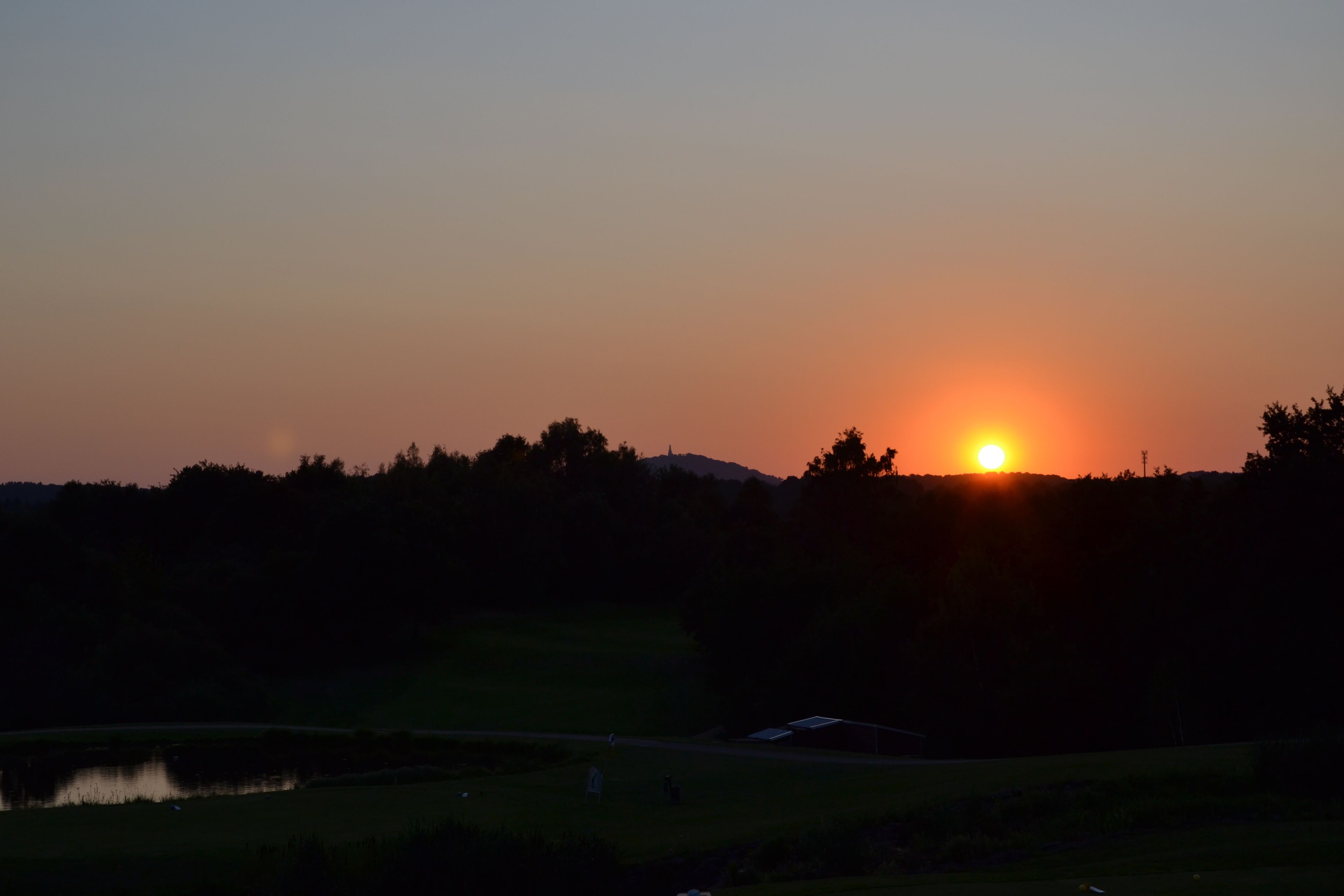 Ein Sonnenuntergang über einer Landschaft mit einem Gewässer und einem kleinen Gebäude.