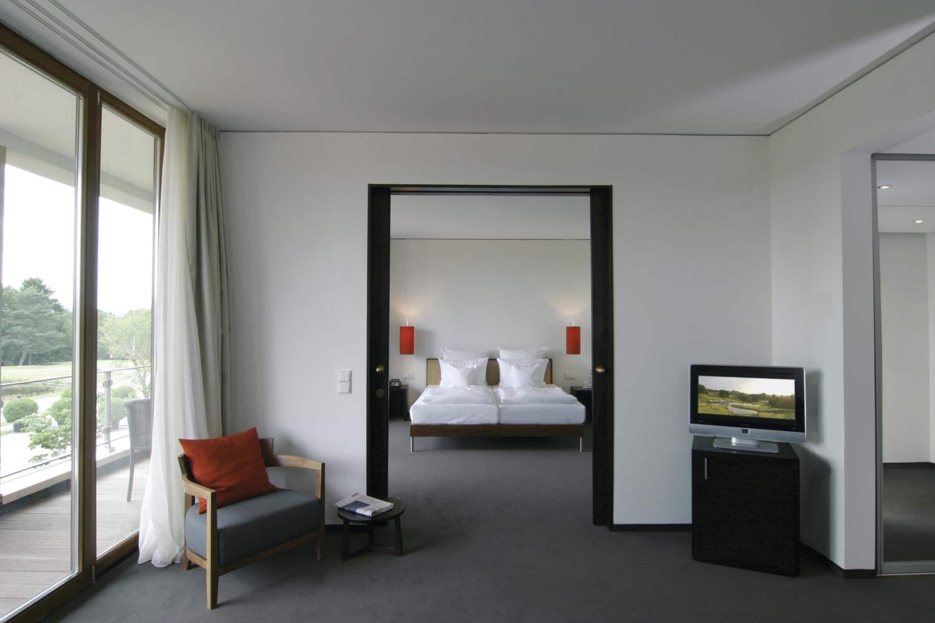 Ein Hotelzimmer mit Bett, Fernseher, Sessel und kleinem Tisch.