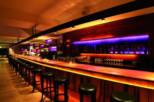 Una zona de bar con una barra larga, varios taburetes y una amplia variedad de botellas.