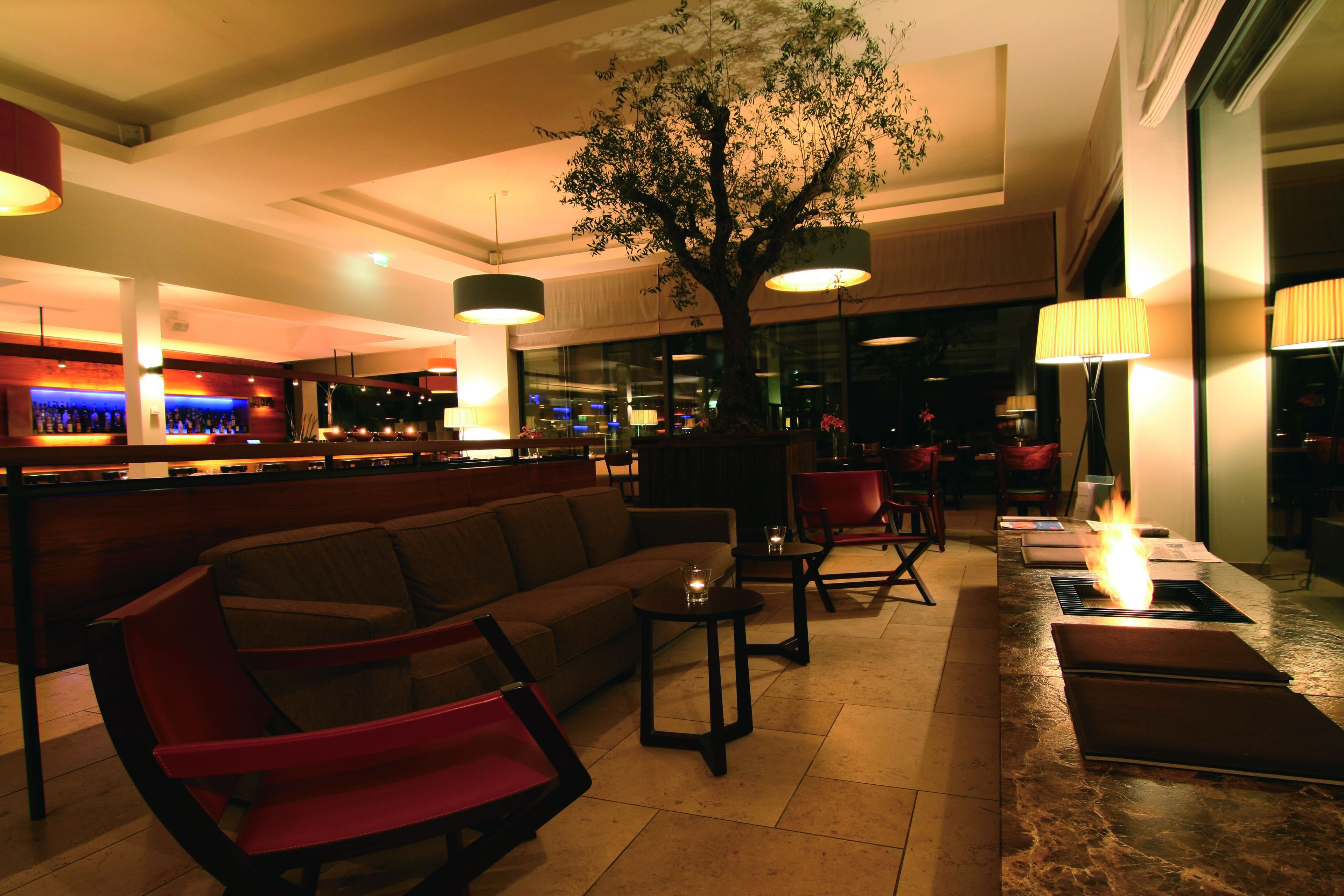 Un área de lounge moderna con asientos, un bar y un gran árbol como elemento central.