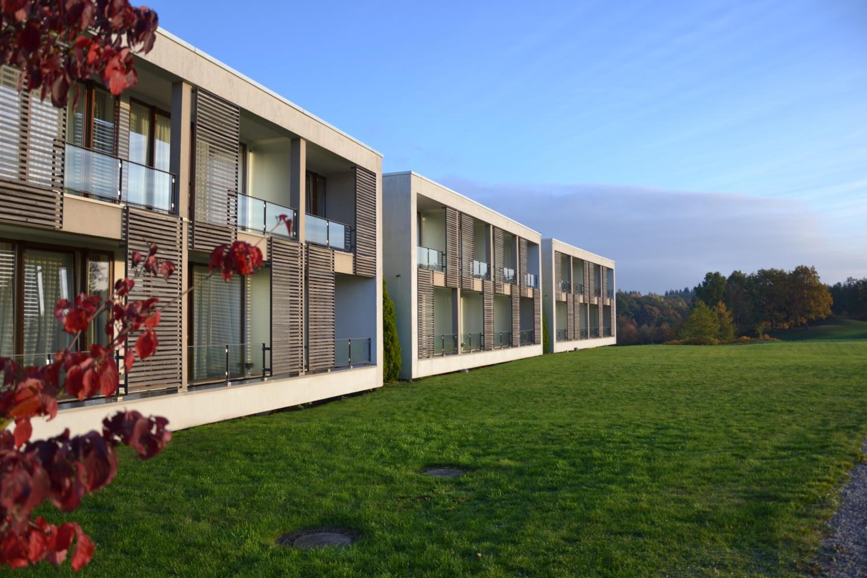 A modern building with multiple balconies and large windows, surrounded by a grassy area.