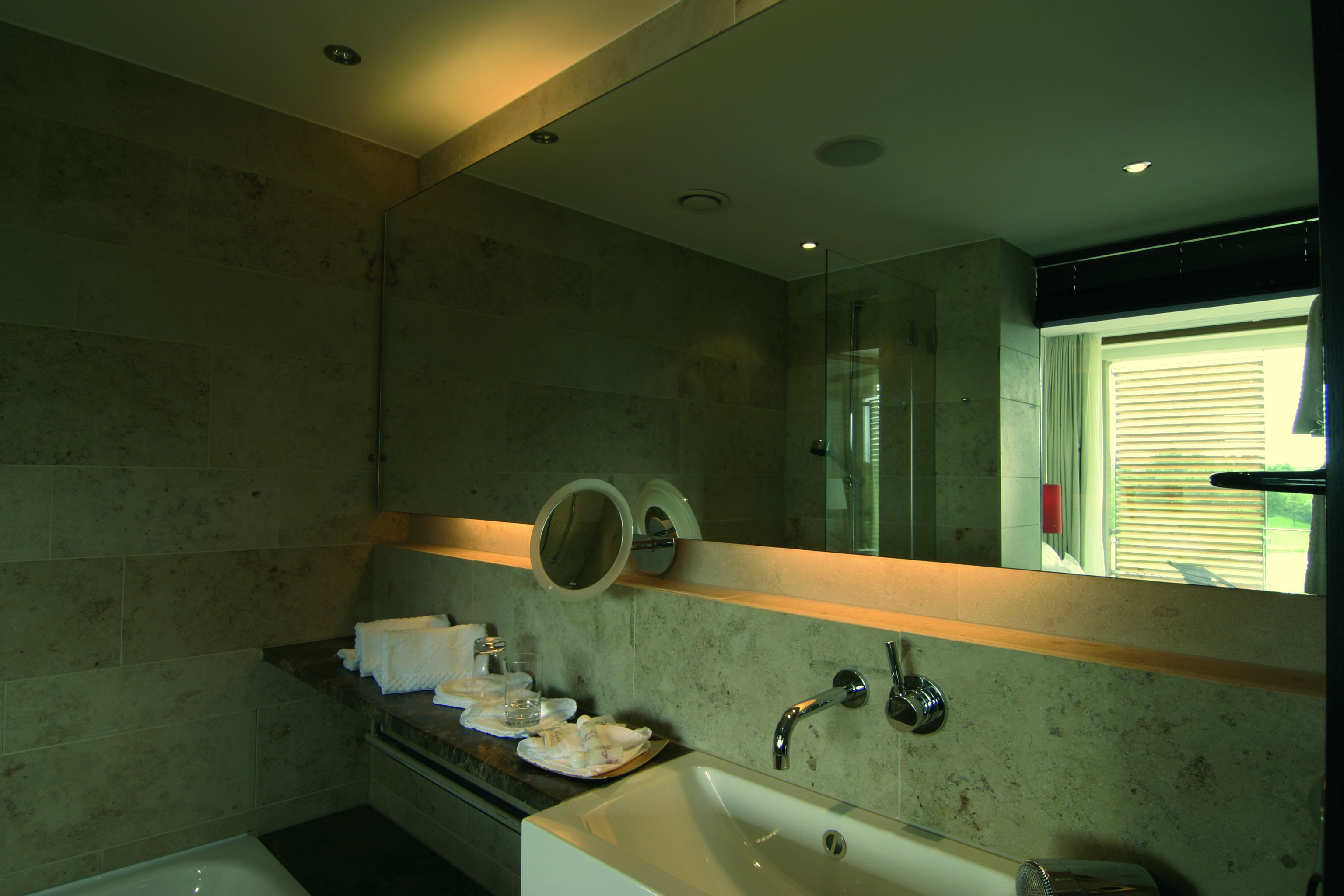 A modern bathroom with a large mirror, a bathtub, and a countertop with toiletries.