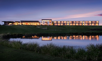 Un hotel moderno con varias edificaciones conectadas, un estanque reflectante y un paisaje cubierto de césped.
