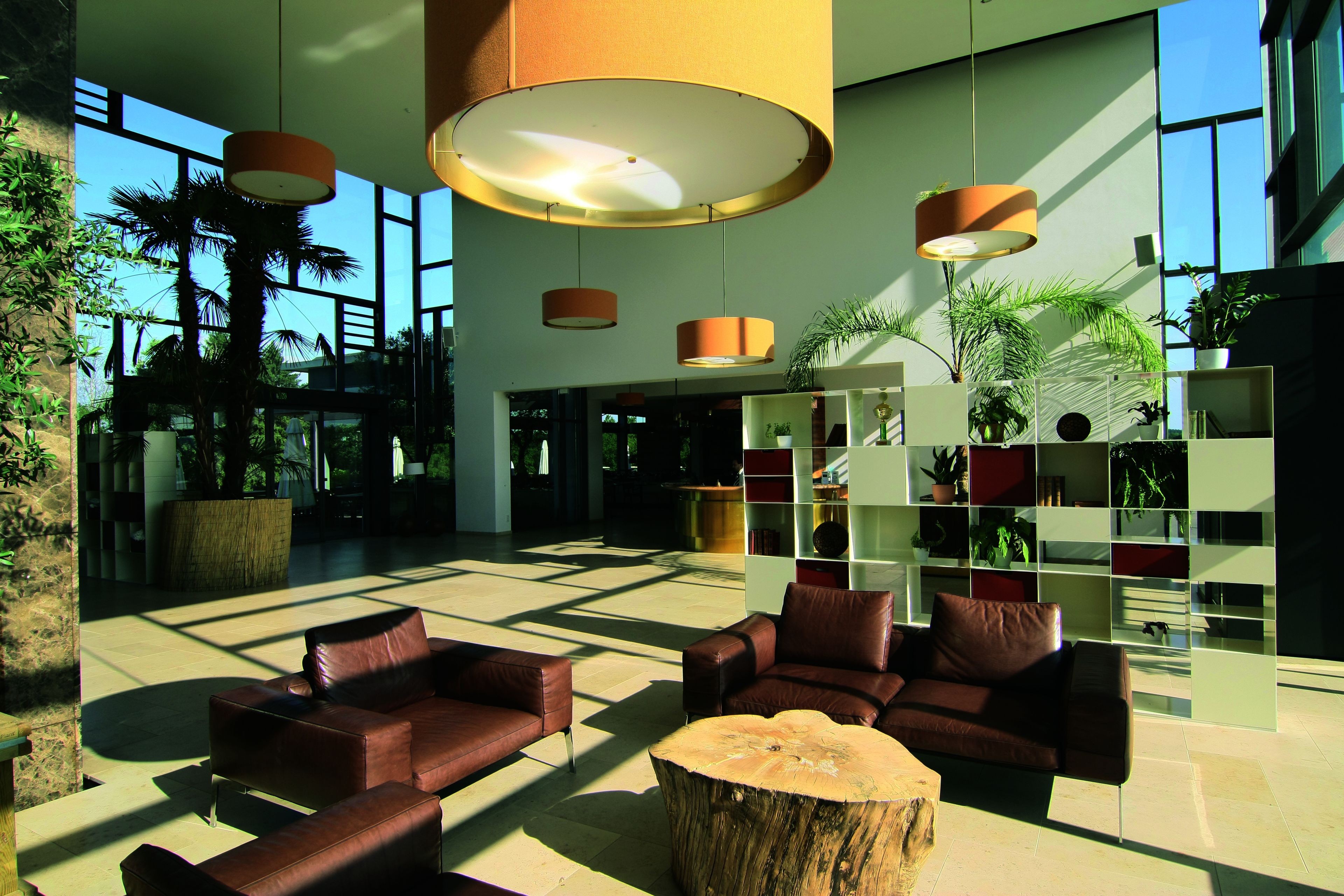 Een ruime lobby met lederen banken, een houten salontafel in het midden en een modern wandrek vol planten.