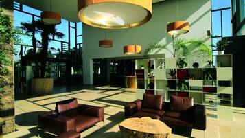 Een ruime lobby met lederen banken, een houten salontafel in het midden en een modern wandrek vol planten.